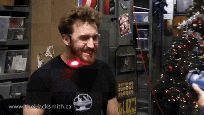 A Man Wearing A Shirt That Says Www.thehacksmith.ca Smiles In Front Of A Christmas Tree GIF