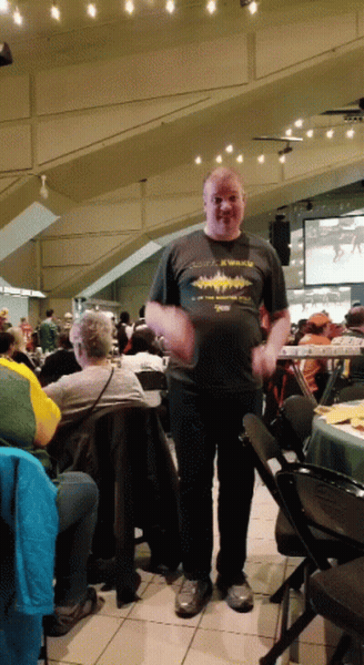A Man Wearing A Shirt That Says X Walks Is Standing In A Crowded Room GIF