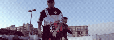 A Man Wearing A Shirt That Says Xxx On It Stands Next To Another Man GIF