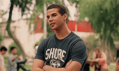 A Man Wearing A Shore T-Shirt Is Standing In A Park With His Arms Crossed GIF