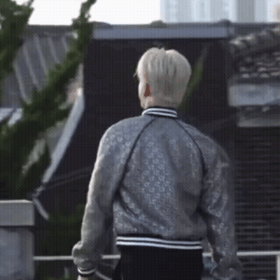 A Man Wearing A Silver Jacket Is Standing In Front Of A Building GIF