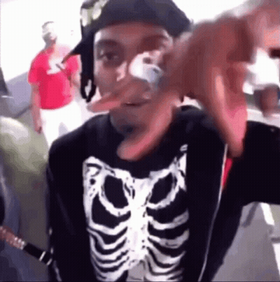 A Man Wearing A Skeleton Shirt And A Hat Is Making A Funny Face GIF