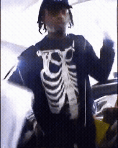 A Man Wearing A Skeleton Shirt Is Standing In Front Of A Car And Giving The Middle Finger . GIF
