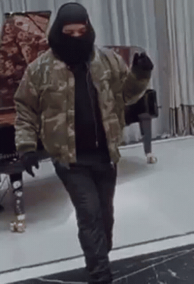 A Man Wearing A Ski Mask And A Camouflage Jacket Is Standing In Front Of A Piano . GIF
