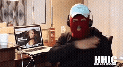 A Man Wearing A Ski Mask Is Sitting In Front Of A Laptop With A Picture Of Roxy Metcalfe On The Screen GIF