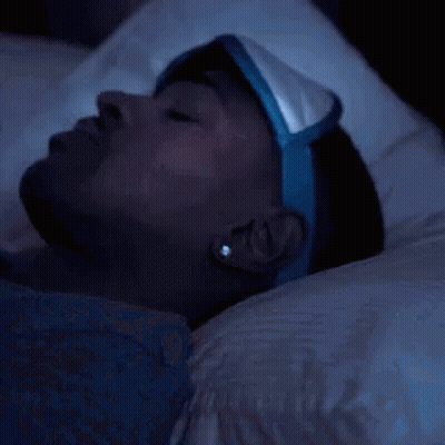 A Man Wearing A Sleep Mask Is Laying In Bed At Night . GIF