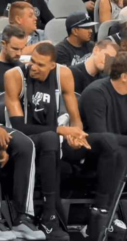 A Man Wearing A Spurs Jersey Sits In The Stands With Other Men GIF