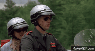 A Man Wearing A State Police Helmet Sits Next To A Woman Wearing Sunglasses GIF