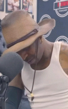 A Man Wearing A Straw Hat And A White Tank Top Looks Down GIF