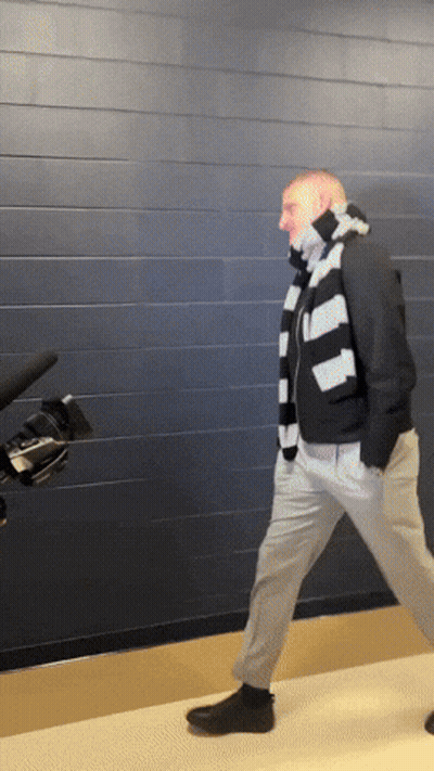 A Man Wearing A Striped Scarf And A Black Jacket Is Walking In Front Of A Camera GIF