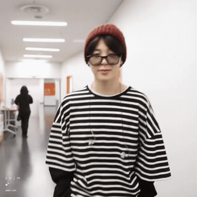 A Man Wearing A Striped Shirt And A Beanie Is Standing In A Hallway GIF