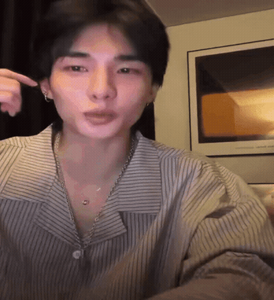 A Man Wearing A Striped Shirt And A Necklace Is Pointing At His Face GIF