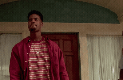 A Man Wearing A Striped Shirt And A Red Shirt Is Standing In Front Of A Door GIF