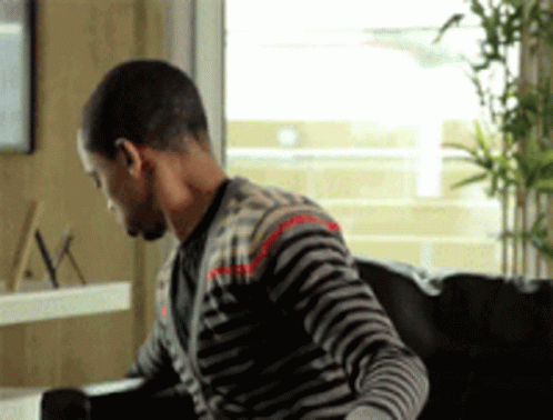 A Man Wearing A Striped Sweater Is Sitting On A Couch GIF