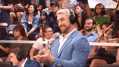 A Man Wearing A Suit And Headphones Is Sitting In A Crowd Watching A Wrestling Match Sponsored By Usa GIF