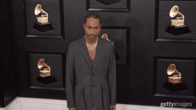 A Man Wearing A Suit And Pearls Stands In Front Of A Wall Of Grammophones GIF