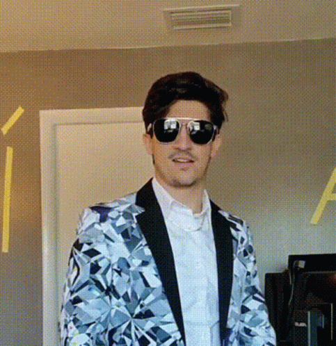 A Man Wearing A Suit And Sunglasses Stands In Front Of A Door GIF