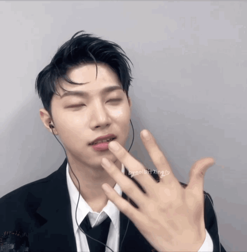 A Man Wearing A Suit And Tie Has His Eyes Closed And His Hand On His Lip GIF