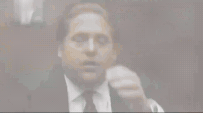 A Man Wearing A Suit And Tie Is Covering His Face With His Hand . GIF