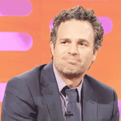 A Man Wearing A Suit And Tie Is Sitting In Front Of An Orange Background . GIF