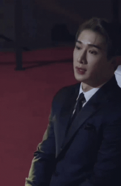 A Man Wearing A Suit And Tie Is Sitting On A Red Carpet . GIF