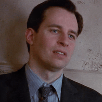 A Man Wearing A Suit And Tie Is Standing In Front Of A Wall . GIF