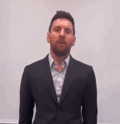 A Man Wearing A Suit And Tie Is Standing In Front Of A White Wall . GIF