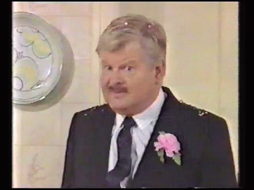 A Man Wearing A Suit And Tie With A Pink Flower In His Lapel GIF
