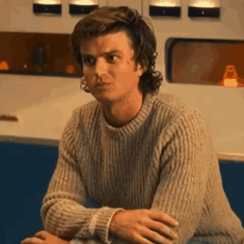 A Man Wearing A Sweater Is Sitting At A Table With His Hands Folded . GIF