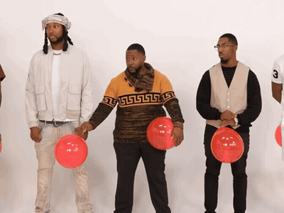 A Man Wearing A Sweater With A Greek Key Design Holds A Red Balloon GIF