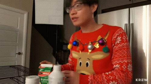 A Man Wearing A Sweater With A Reindeer On It Is Standing In Front Of A Refrigerator GIF