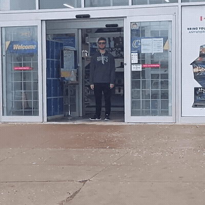 A Man Wearing A Sweatshirt That Says Roots Stands In Front Of A Store GIF