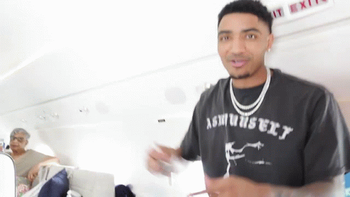 A Man Wearing A T-Shirt That Says Ashbury Is Standing In Front Of An Exit Sign . GIF