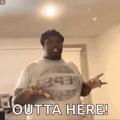 A Man Wearing A T-Shirt That Says Outta Here Is Standing In A Room With His Hands Outstretched . GIF