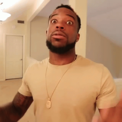 A Man Wearing A Tan T-Shirt And A Gold Necklace With A Dog Tag On It Looks Surprised GIF
