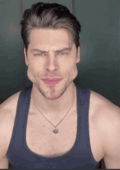 A Man Wearing A Tank Top And A Necklace Is Making A Face . GIF