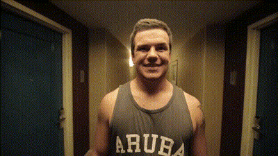 A Man Wearing A Tank Top That Says Aruba Smiles In A Hallway GIF