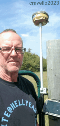 A Man Wearing A Tech @ Hellyeah Shirt Stands In Front Of A Pole GIF