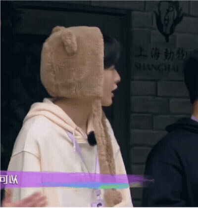 A Man Wearing A Teddy Bear Hat Is Standing In Front Of A Shanghai Sign . GIF