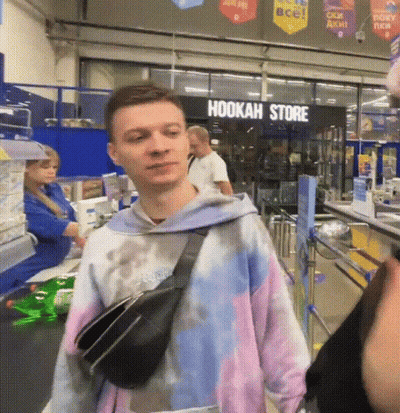 A Man Wearing A Tie Dye Sweatshirt Is Standing In Front Of A Hookah Store GIF