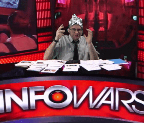 A Man Wearing A Tin Foil Hat Sits At A Desk In Front Of A Sign That Says Info Wars GIF