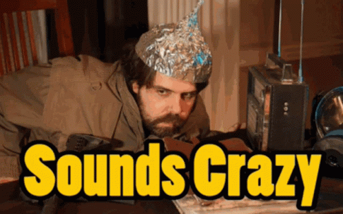 A Man Wearing A Tin Foil Hat Sits At A Table With The Words " Sounds Crazy " In Yellow Letters GIF