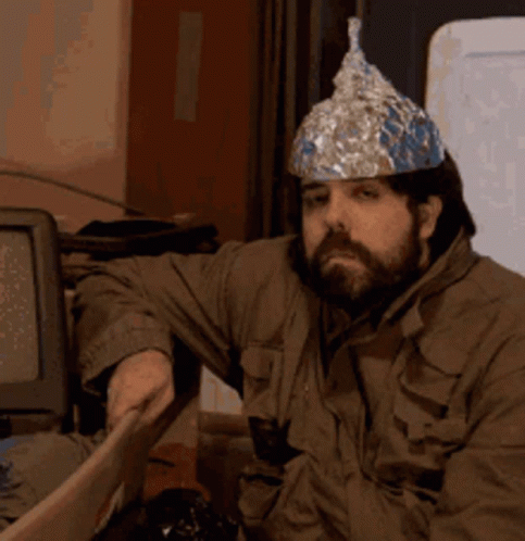 A Man Wearing A Tin Foil Hat Sits In Front Of A Computer Monitor GIF