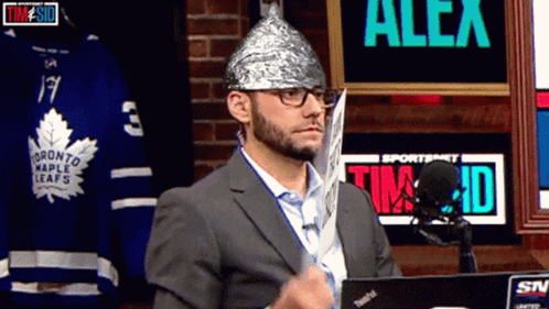 A Man Wearing A Tin Foil Hat Stands In Front Of A Sign That Says Alex On It GIF