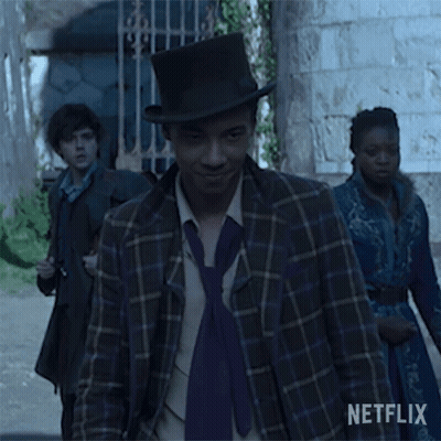 A Man Wearing A Top Hat And A Purple Tie Is Walking Down The Street . GIF