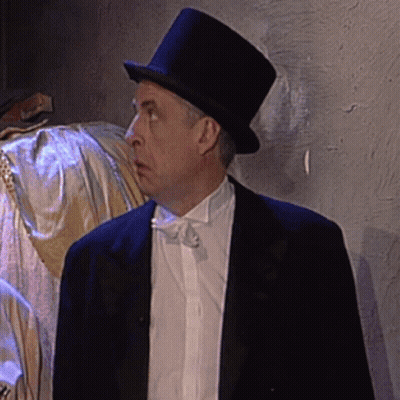 A Man Wearing A Top Hat And A Tuxedo Looks To The Side GIF