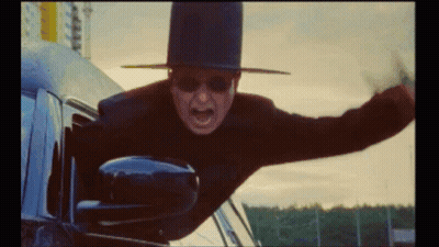 A Man Wearing A Top Hat And Sunglasses Is Flying Out Of A Car Window GIF