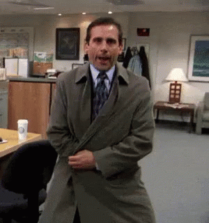 A Man Wearing A Trench Coat And Tie Is Standing In A Room . GIF