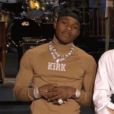 A Man Wearing A Turtleneck And A Necklace With The Name Kirk On It Is Standing In Front Of A Drum Set . GIF