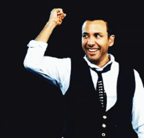 A Man Wearing A Vest And Tie Holds His Fist Up In The Air GIF